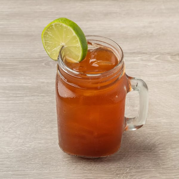 Iced tea in a mason jar with a lime wedge on a light wooden table.