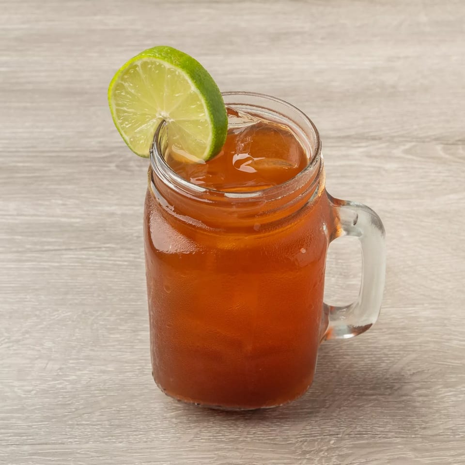 Iced tea in a mason jar with a lime wedge on a light wooden table.