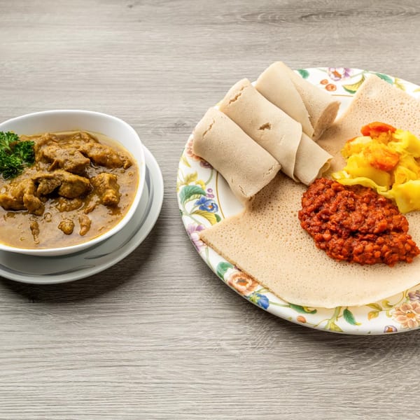 Ethiopian injera bread with red lentil stew, yellow cabbage, and a bowl of meat stew.