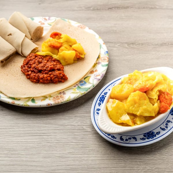 Ethiopian injera bread with red lentil stew and yellow vegetable curry on a wooden table.