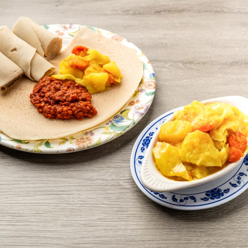 Ethiopian injera bread with red lentil stew and yellow vegetable curry on a wooden table.