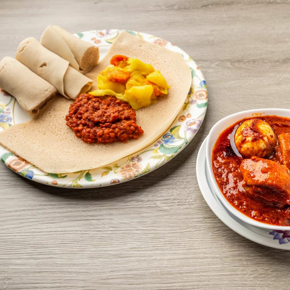 Ethiopian injera bread with red lentil stew, yellow cabbage, and a bowl of Doro Wat.