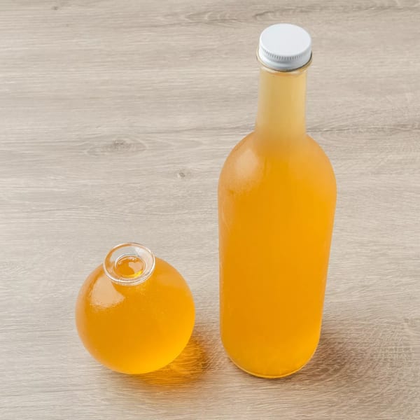 Two bottles of Ethiopian honey wine, one tall and one round, on a light wooden surface.