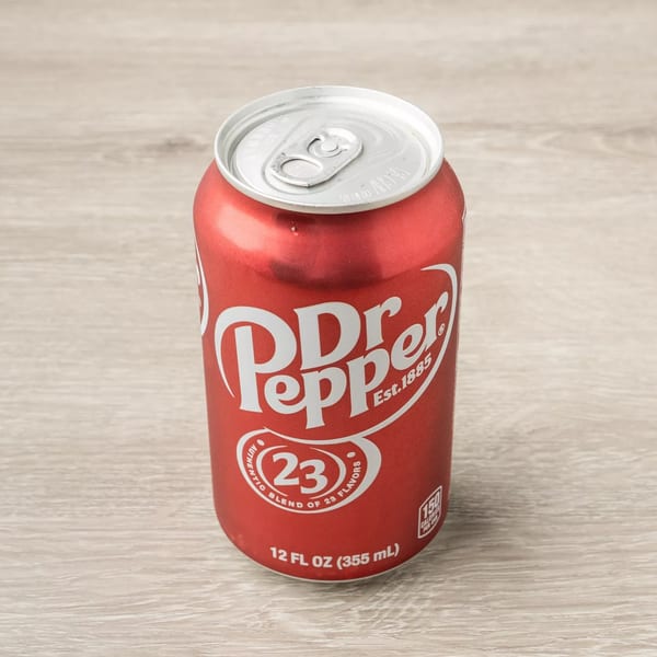 A red Dr. Pepper soda can with a silver top sits on a light wooden surface.