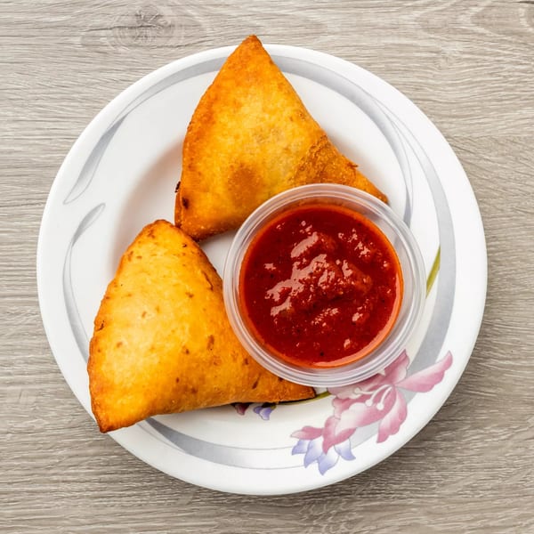 Two golden-fried Ethiopian sambusas and a small cup of red dipping sauce on a white plate.