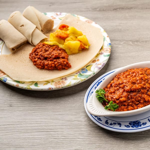 Ethiopian injera bread with red lentil stew and yellow vegetable stew, plus a side of red lentil stew.